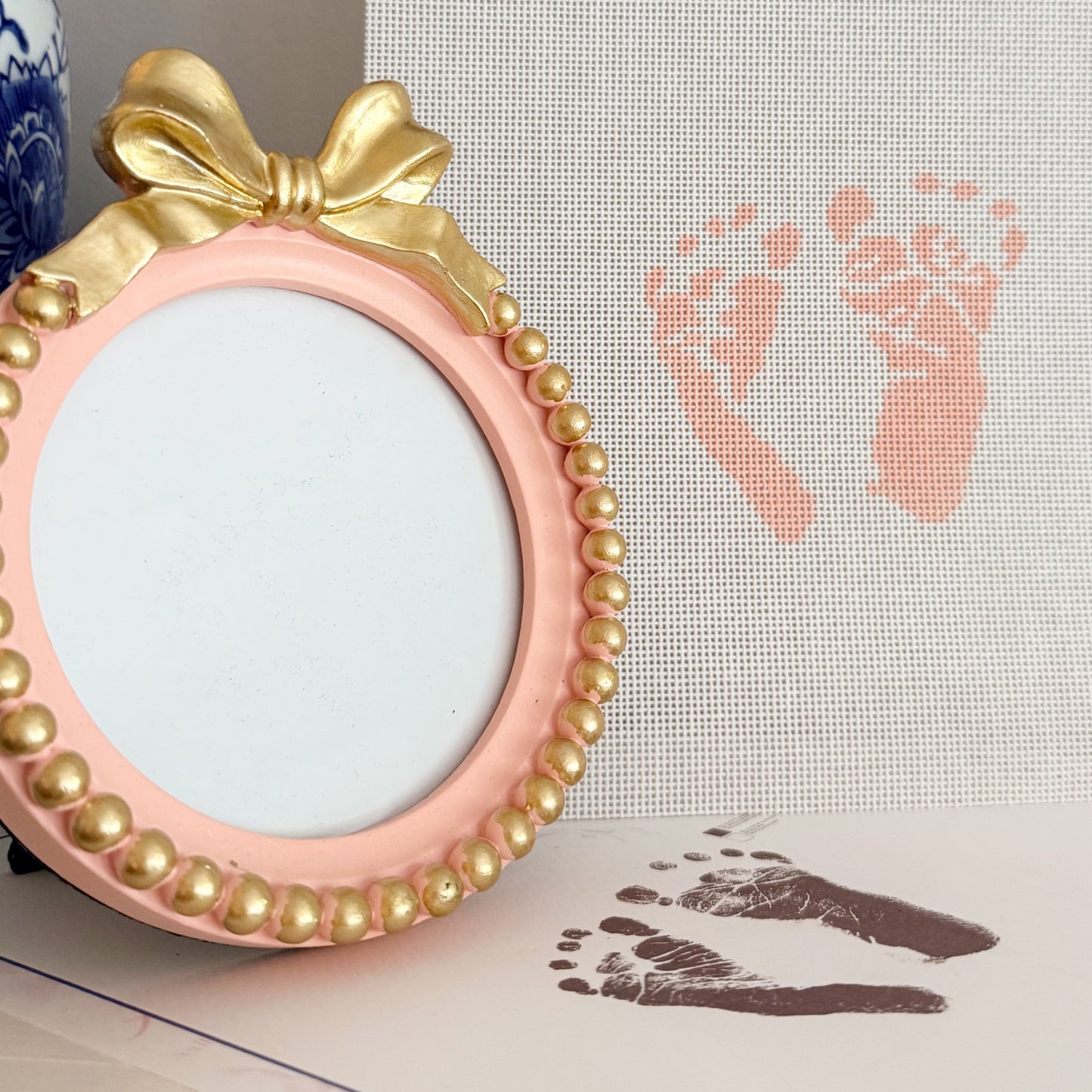 Hand-painted custom newborn footprint needlepoint canvas featuring baby’s actual footprints, displayed with a pink bow keepsake frame for a timeless heirloom gift.