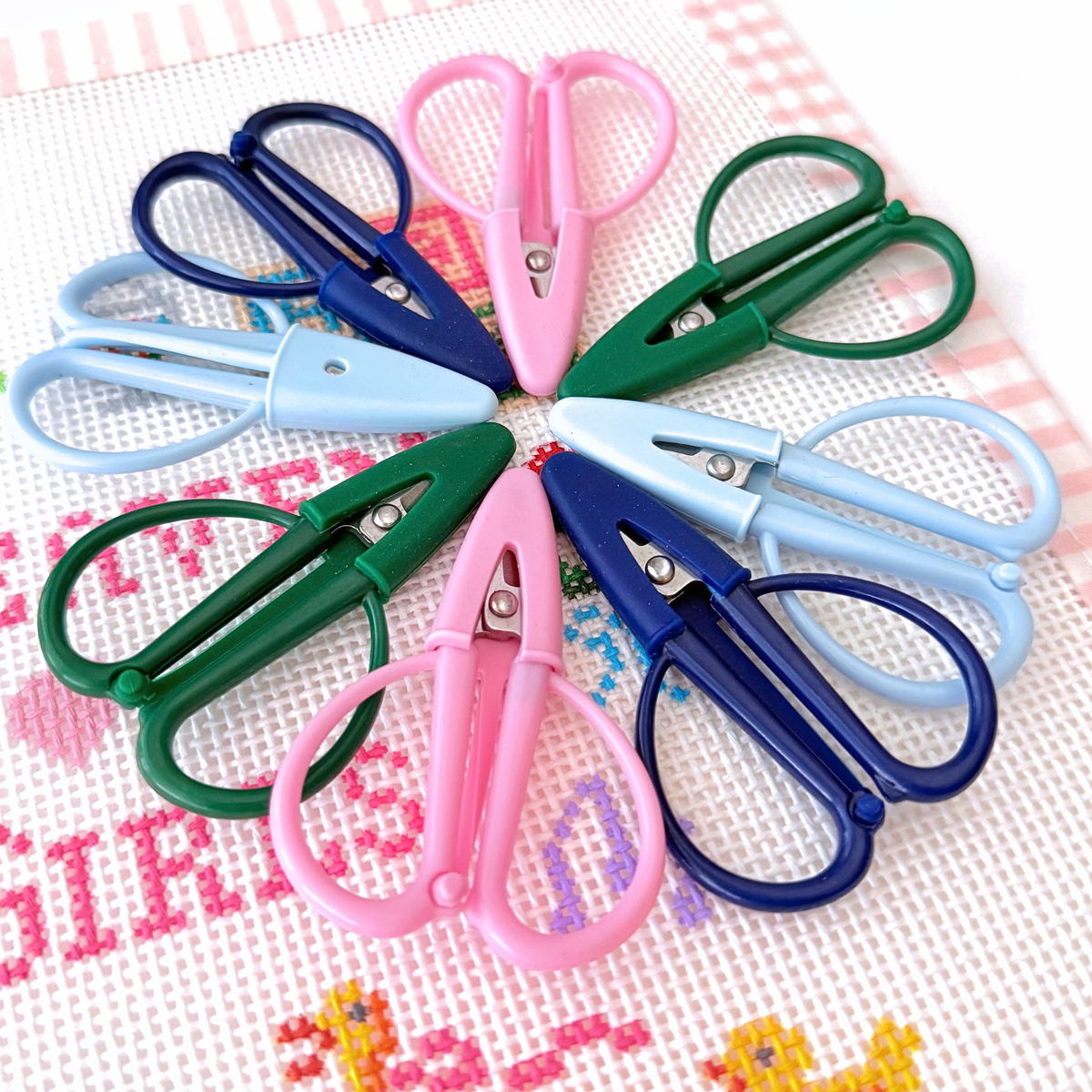 Colorful mini needlepoint snips with protective blade covers displayed on a stitched canvas