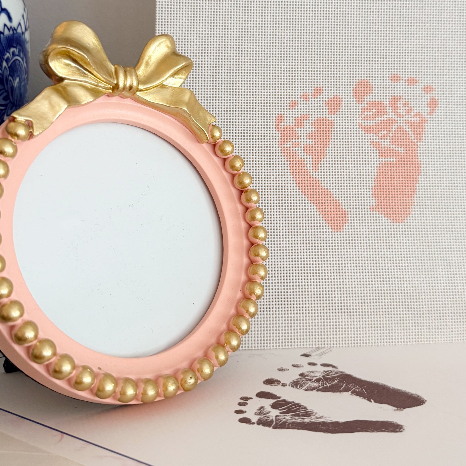 Hand-painted custom newborn footprint needlepoint canvas featuring baby’s actual footprints, displayed with a pink bow keepsake frame for a timeless heirloom gift.
