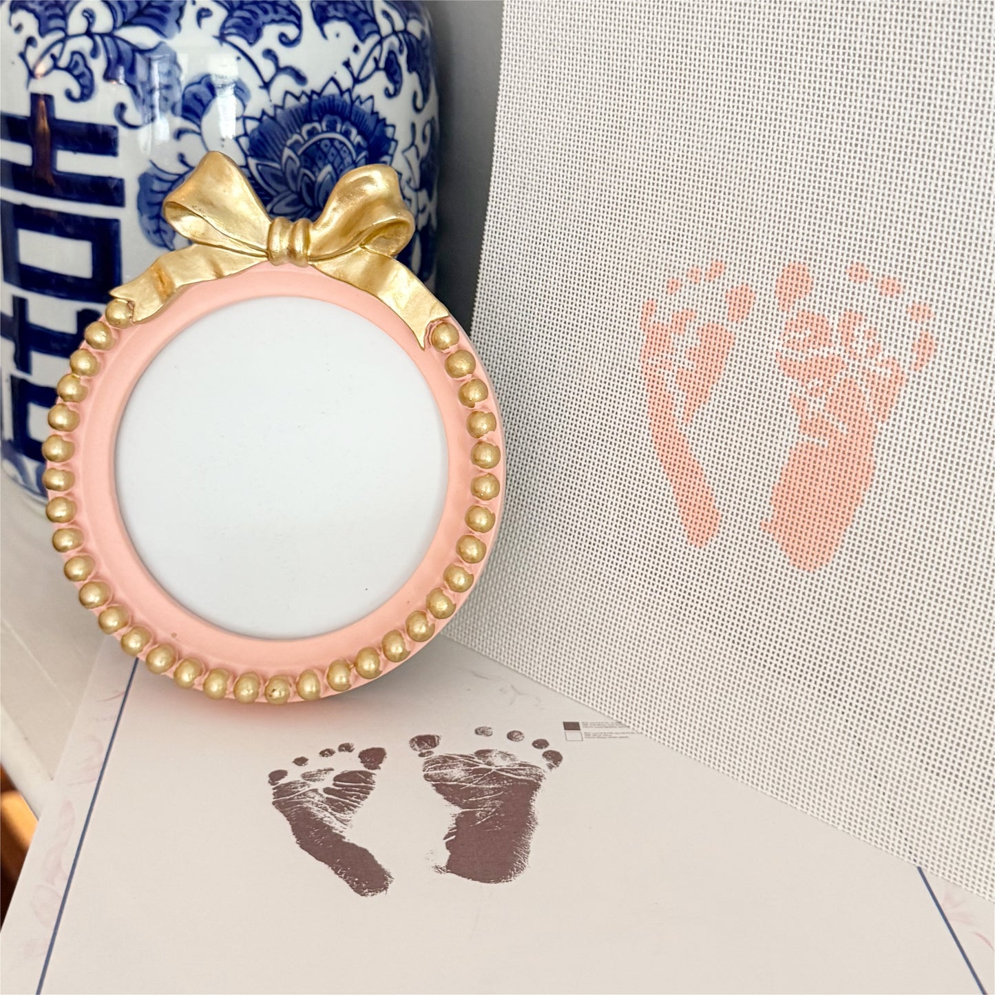 Custom newborn footprint needlepoint canvas hand-painted on 18 count canvas beside a pink and gold keepsake frame using a baby’s actual footprints.