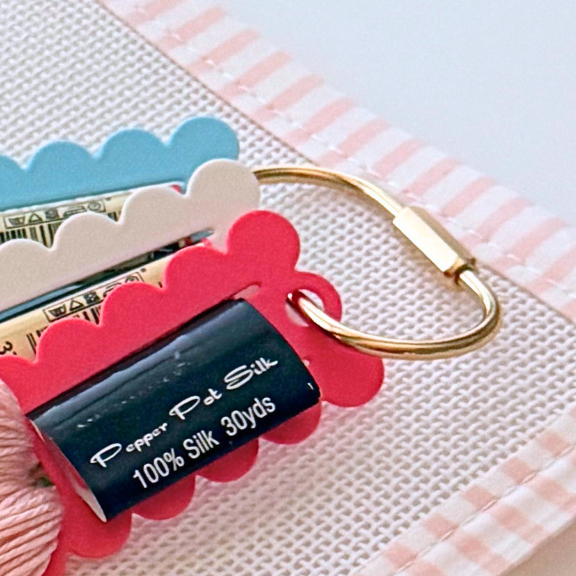 Needlepoint thread organizer ring with brass carabiner attached to floss drops.